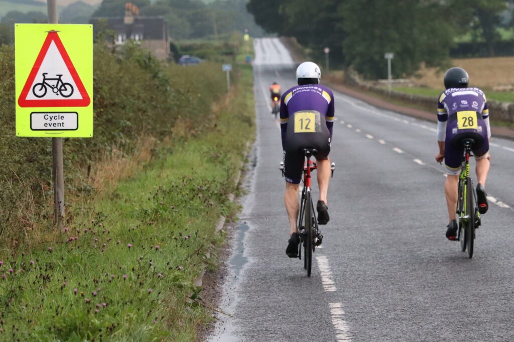 Two Kinross Cycling Club members riding away along a road after an FCA Midweek Time Trial event.